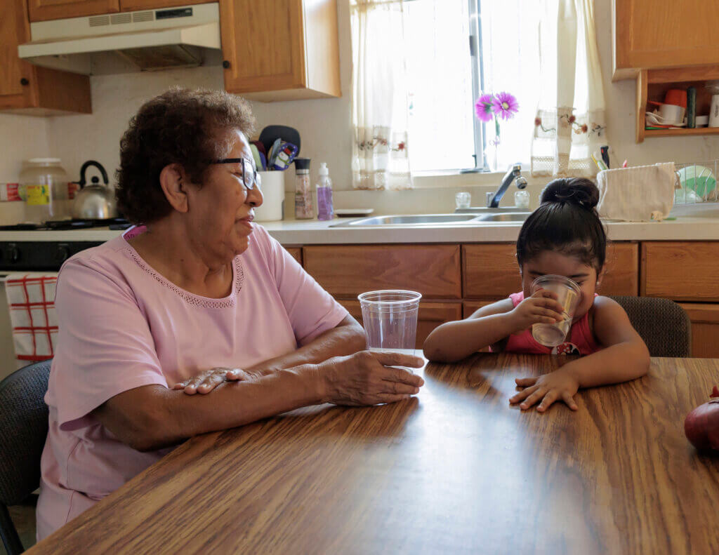 A grandmother and her granddaughter sitting at the kitchen table together, each has a glass of clean drinking water in their hands